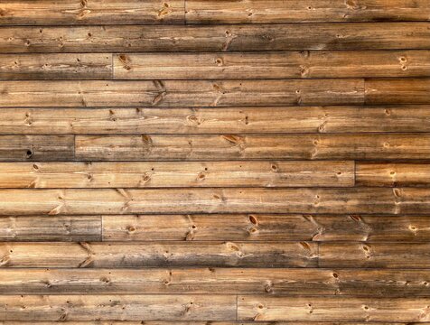A full-frame background of a rustic wooden wall made of horizontal logs. The weathered timber logs feature natural textures, knots, and a mix of light brown and dark aged wood grain, creating a warm, 