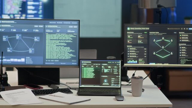 Zoom out shot of cybersecurity workstation with multiple monitors and laptop displaying network analysis, coding interface and digital security in modern office