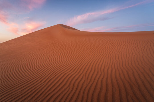 View of the Eastern Sands desert dunes with wind-blown ripples under a colorful sunset sky in Oman.