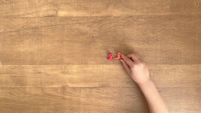 child hands placing two small colorful clips in a row on wooden table slow motion 4K