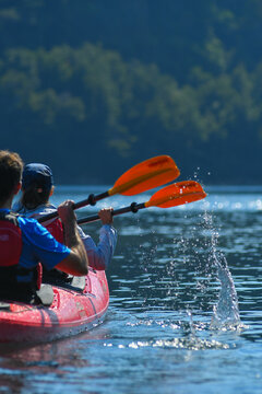View of people paddling a red kayak on the blue waters of Nahuel Huapi Lake with forested hills in the background San Carlos de Bariloche, Rio Negro, Argentina.