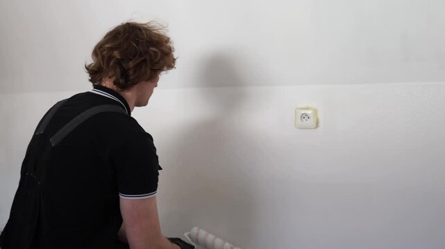 Man painting white apartment wall with roller during home renovation careful interior improvement and modern residential repair process indoors