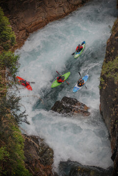 View of kayakers navigating the white water rapids of Rio Manso through a narrow rocky canyon with lush vegetation in San Carlos de Bariloche, Rio Negro, Argentina.