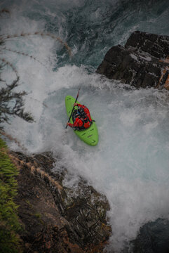 View of a kayaker in a green boat navigating the white water rapids of the Rio Manso surrounded by dark rocks in San Carlos de Bariloche, Rio Negro, Argentina.
