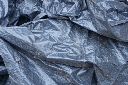 Plastic texture of a piece of dirty crumpled black cellophane in the street