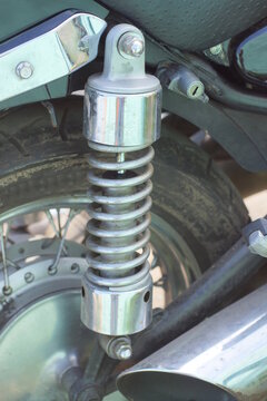 part of a sports motorcycle with a  wheel and a white gray metal chrome spring on the street