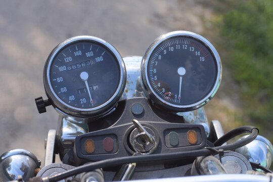 two black round plastic speedometer on the dashboard of an old motorcycle on a summer street