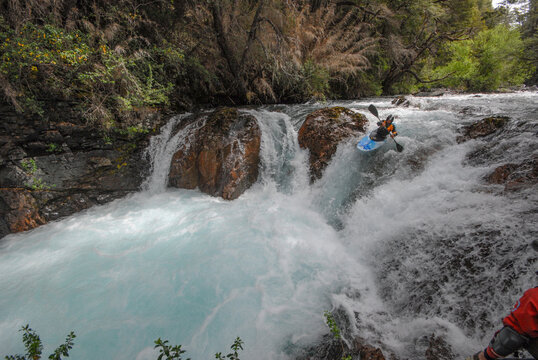 View of a kayaker navigating the turquoise rapids of the Rio Manso waterfall surrounded by lush forest in San Carlos de Bariloche, Rio Negro, Argentina.