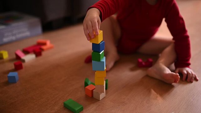 Toddler building tower from colorful wooden blocks on floor at home. Educational game and early childhood development concept.