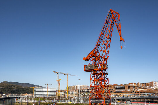 View of the iconic red Carola Crane at the Itsasmuseum Bilbao with urban buildings and a clear blue sky in Greater Bilbao, Basque Country, Spain.