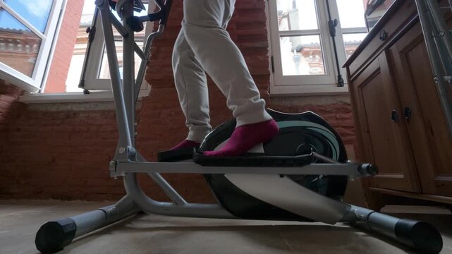 man exercising on elliptical trainer at home near window fitness cardio workout