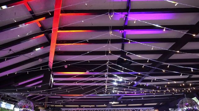 Electric garland under the roof of the summer veranda with wooden beams. Flashing lights of garlands and spotlights on the ceiling.