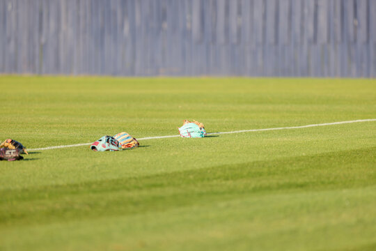 Multiple baseball gloves and baseballs rest on the grass beside a painted field line during pregame warmups at a high school baseball game in Olive Branch, Mississippi.