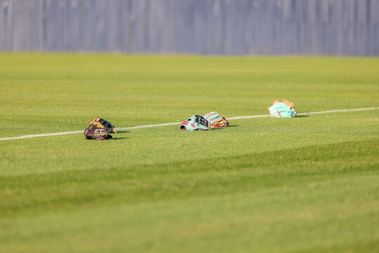 Multiple baseball gloves and baseballs rest on the grass beside a painted field line during pregame warmups at a high school baseball game in Olive Branch, Mississippi.