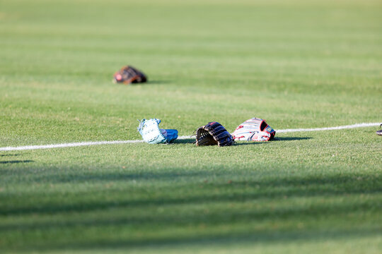 Multiple baseball gloves and baseballs rest on the grass beside a painted field line during pregame warmups at a high school baseball game in Olive Branch, Mississippi.
