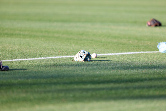 Multiple baseball gloves and baseballs rest on the grass beside a painted field line during pregame warmups at a high school baseball game in Olive Branch, Mississippi.