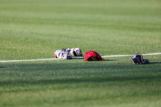Multiple baseball gloves and baseballs rest on the grass beside a painted field line during pregame warmups at a high school baseball game in Olive Branch, Mississippi.