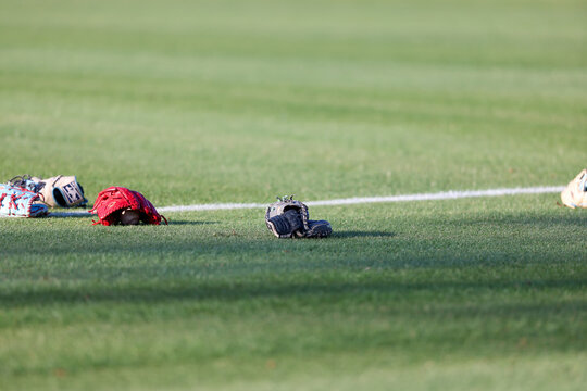 Multiple baseball gloves and baseballs rest on the grass beside a painted field line during pregame warmups at a high school baseball game in Olive Branch, Mississippi.