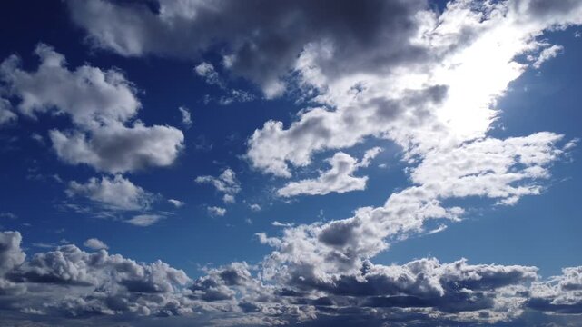 Cinematic aerial view of white fluffy clouds moving across a deep blue sky, bright sun shining through clouds, peaceful nature background, high-altitude drone footage, cloudscape.