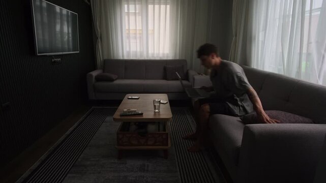 Remote worker changing positions around apartment while working on laptop, authentic freelance routine and modern digital lifestyle in small living space