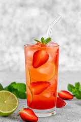 Fototapeta premium Glass of strawberry lemonade with lime slices and mint leaves. Cold summer drink. Copy space.