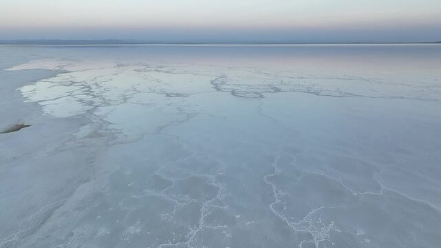 Aerial view of the white salt crust and shallow water reflections of the Danakil Desert under a soft dawn sky in Dalol, Afar, Ethiopia.