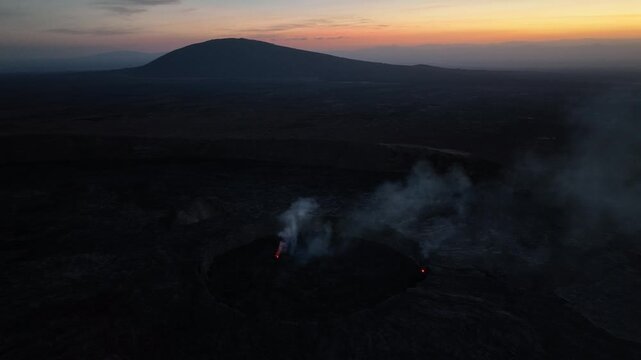 Aerial view of the Danakil Desert volcanic crater with rising smoke and steam under a colorful dusk sky Dalol, Afar, Ethiopia.