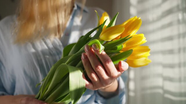 Woman holding bouquet of yellow tulips indoors as romantic floral gift symbolizing love, care, tenderness, and celebration of special emotional moments.