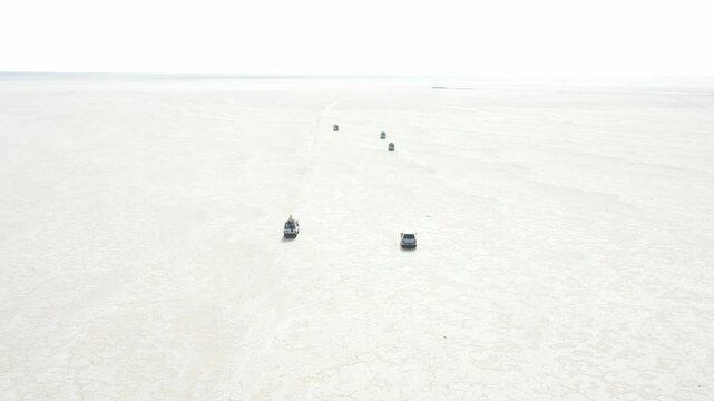 Aerial view of off-road vehicles driving across the vast white salt flats of the Danakil Desert under a bright sky in Dalol, Afar, Ethiopia.