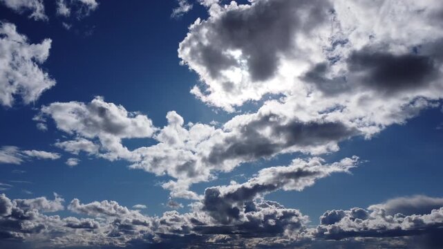 Cinematic 4K aerial view of bright sun shining behind white fluffy clouds, deep blue sky with moving cloudscape, backlit nature background, high altitude drone footage, atmospheric sky