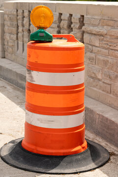 Orange road barrel featuring two reflective white bands and a small amber light on top, used for demarcating construction zones and ensuring safety