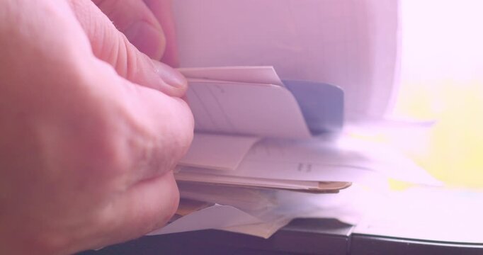 The hands of a man searching for a document in a stack of papers illuminated by the morning light from a window. Paperwork. Information search. Close-up shot from a low angle.