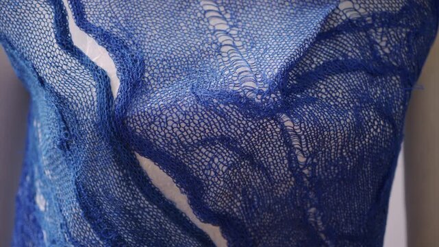 Close up of a blue openwork knitted textile stretched over a white form