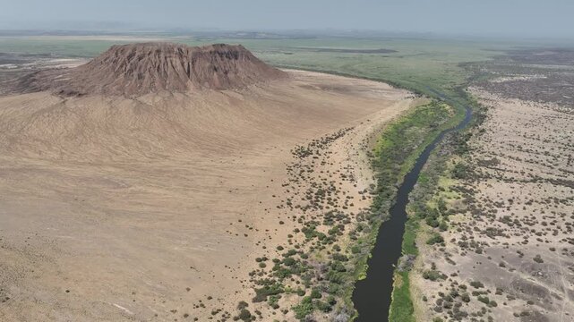 Aerial view of the Danakil Desert featuring a volcanic crater and a river with lush green banks flowing through the arid landscape in Dalol, Afar, Ethiopia.