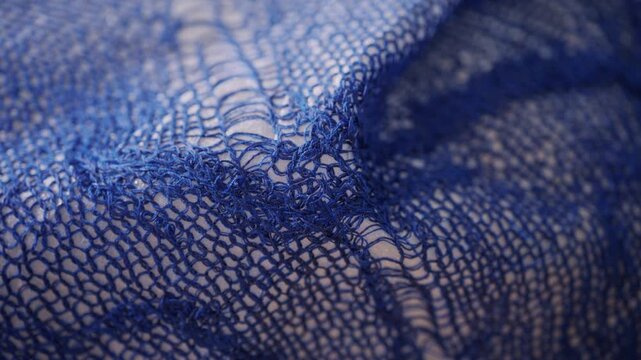 Close up of a blue openwork knitted textile stretched over a white form