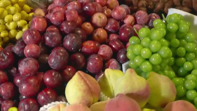 Exotic fruits - red plums, green grapes, yellow langsat and brown spiky snake fruit (salak) are sold on the market stall in Da Lat Night Market, Vietnam
