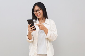 Fototapeta premium A beautiful young Asian woman is using a mobile phone, laughing while pointing at the phone screen, searching for interesting apps or getting good news via mobile phone.