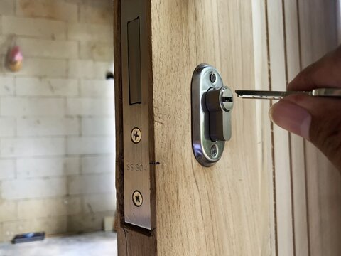 Hand inserting key into modern door lock cylinder on wooden door. locksmith installation.