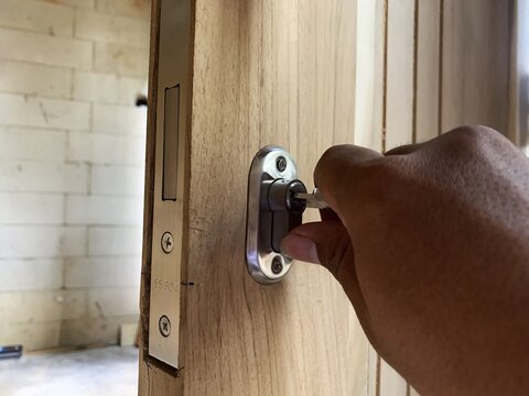 Hand inserting key into modern door lock cylinder on wooden door. DIY renovation.