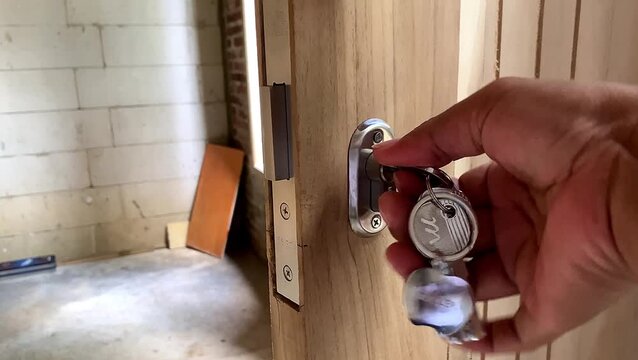 Hand inserting key into modern door lock cylinder on wooden door. home security.