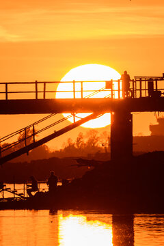 Golden hour backlight silhouette of a bridge and angler fishing at sunset.