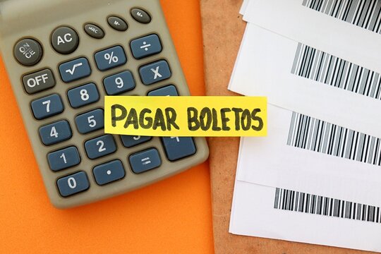 Post-it note with the words "Pagar Boletos" (bill payment, in Portuguese) next to bills with barcodes (c&oacute;digo de barras), computer and a calculator. 