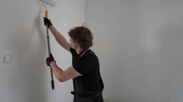 Young man repainting apartment walls with roller during home renovation creating fresh clean interior in empty room with focused repair process atmosphere