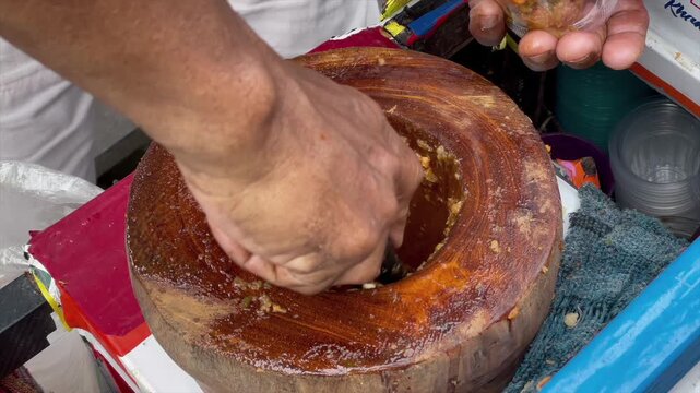 Making traditional indonesian crushed fruit salad known as rujak beubeuk inside a wooden mortar