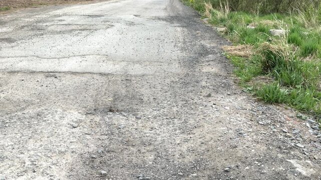 Gravel road pothole damage daytime closeup of rutted asphalt and scattered rubble showing cracked surface texture, uneven patches
