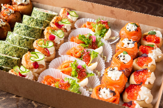 An assortment of gourmet appetizers and canapes with salmon, caviar, and shrimp beautifully arranged in a catering box.