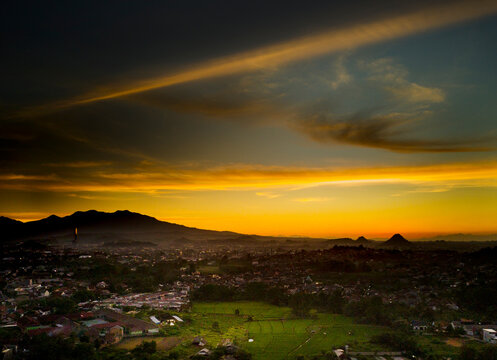 Dramatic golden sunset with sun rays breaking through dark storm clouds over a city landscape at Bandar Lampung