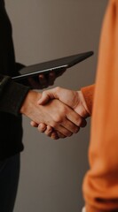 Naklejka premium Two people shake hands while one holds a tablet. This is a business deal or partnership agreement. They might be colleagues discussing work.