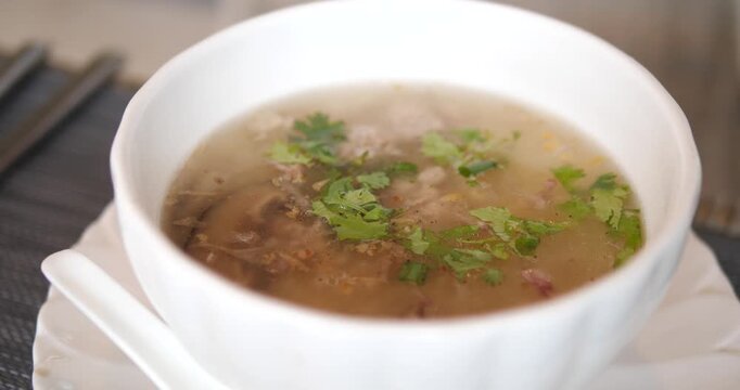 Cinematic close-up of hot traditional Thai rice soup (Khao Tom) served in a white ceramic bowl, morning breakfast and asian comfort food concept