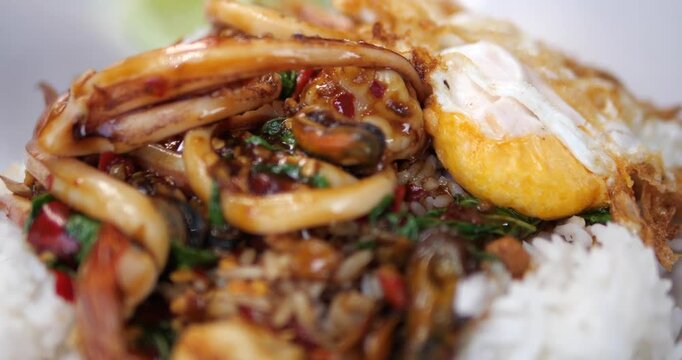 Cinematic close-up of traditional Thai stir-fried seafood with holy basil (Pad Kra Prow Talay) served over steamed rice with a crispy fried egg
